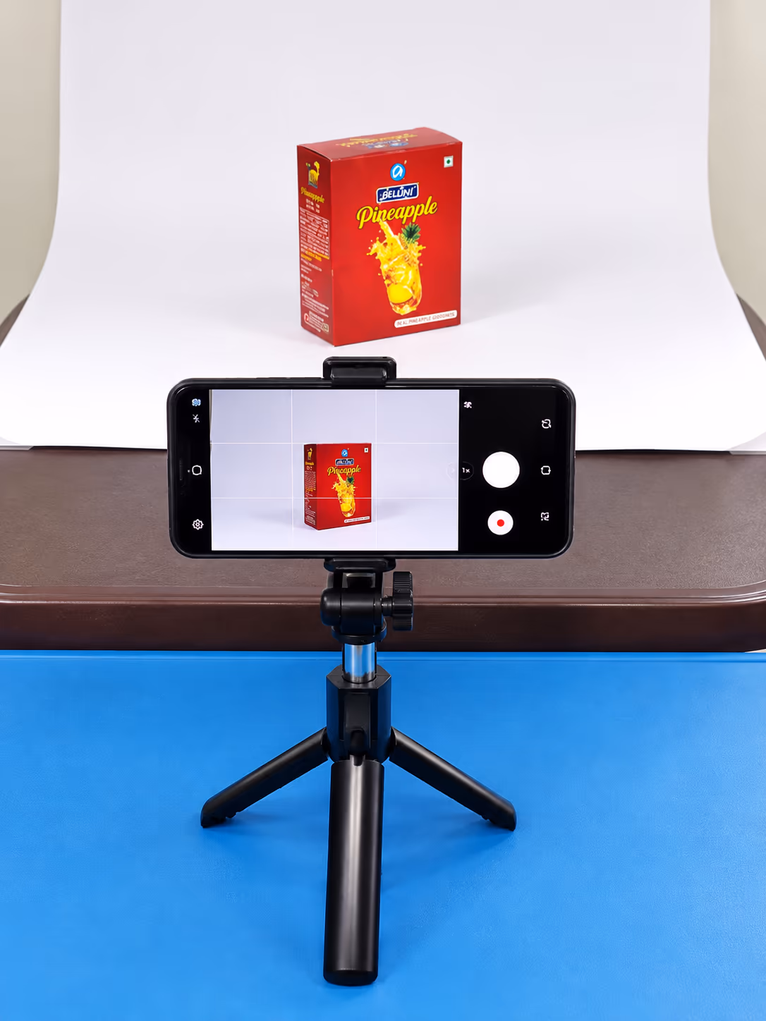 Behind the scenes: phone on a tripod photographing an Antller pineapple pack on a white seamless backdrop